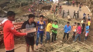 ​Residents, volunteers, and members of the military work together to carry the DSWD family food packs across the torn-down Dalama Bridge in Munai, Lanao del Norte.